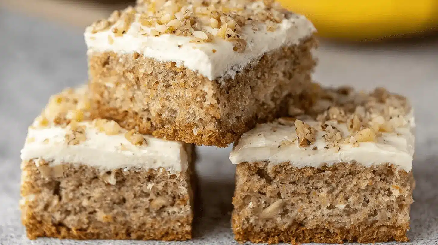 Irresistibly Moist Banana Cake Recipe with Cream Cheese Frosting 1 Delicious square pieces of moist banana cake with creamy frosting and walnuts, perfect for a homemade banana cake recipe.